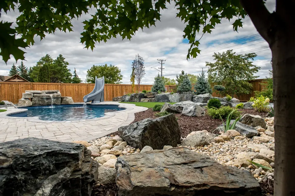 Backyard pool landscape with boulders, artificial turf, garden beds and stepping stones